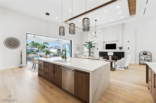 kitchen with pendant lighting, sink, a kitchen island with sink, light stone counters, and stainless steel dishwasher