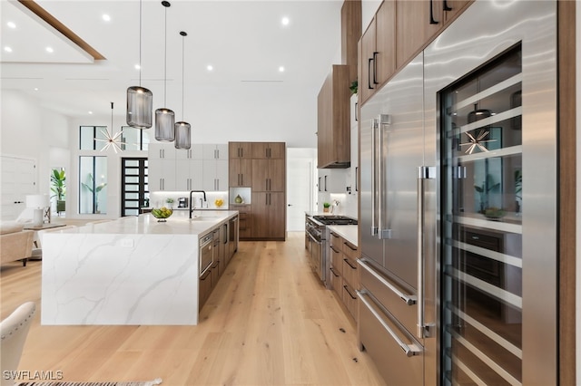 kitchen with high end appliances, hanging light fixtures, light stone countertops, and sink