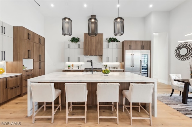 kitchen with hanging light fixtures, built in fridge, light stone countertops, a kitchen island with sink, and white cabinets