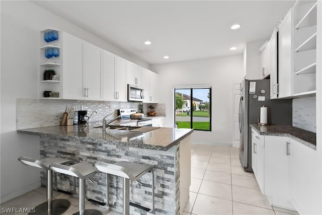 kitchen featuring appliances with stainless steel finishes, dark stone countertops, backsplash, white cabinets, and kitchen peninsula