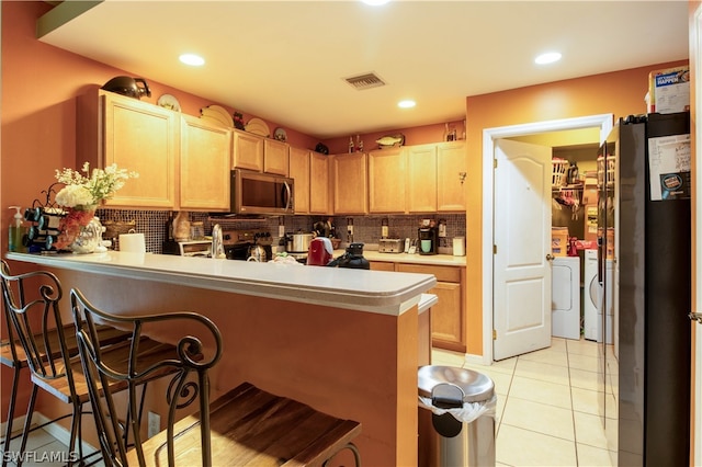 kitchen featuring appliances with stainless steel finishes, kitchen peninsula, light tile patterned floors, decorative backsplash, and washer and dryer