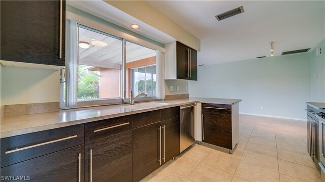 kitchen with light tile patterned flooring, sink, dark brown cabinets, stainless steel dishwasher, and kitchen peninsula