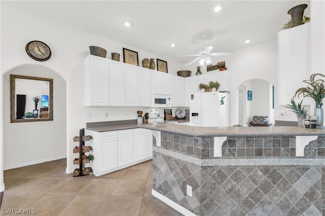 kitchen featuring white appliances, a kitchen breakfast bar, light tile patterned floors, ceiling fan, and white cabinetry