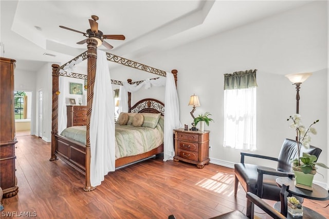 bedroom with ceiling fan, multiple windows, hardwood / wood-style flooring, and a tray ceiling