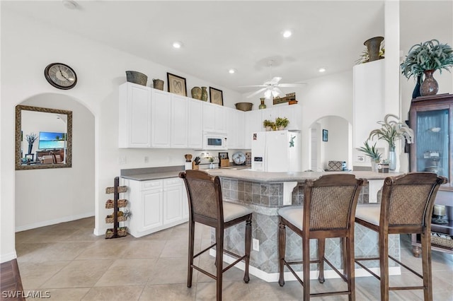 kitchen with white cabinetry, white appliances, a kitchen bar, ceiling fan, and light tile patterned floors