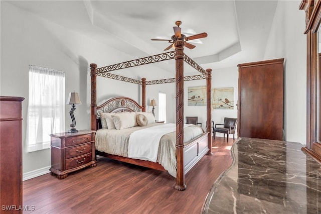 bedroom with ceiling fan, dark hardwood / wood-style flooring, multiple windows, and a tray ceiling