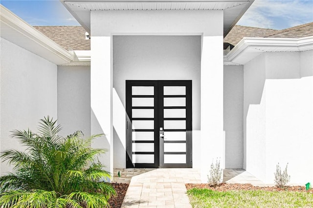 doorway to property featuring roof with shingles and stucco siding