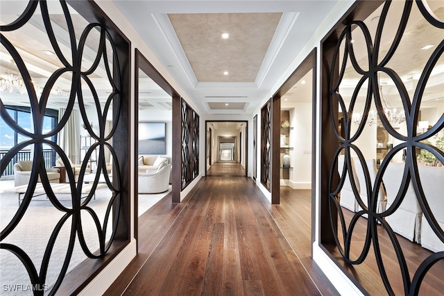 hall featuring dark wood-type flooring, a tray ceiling, and a chandelier