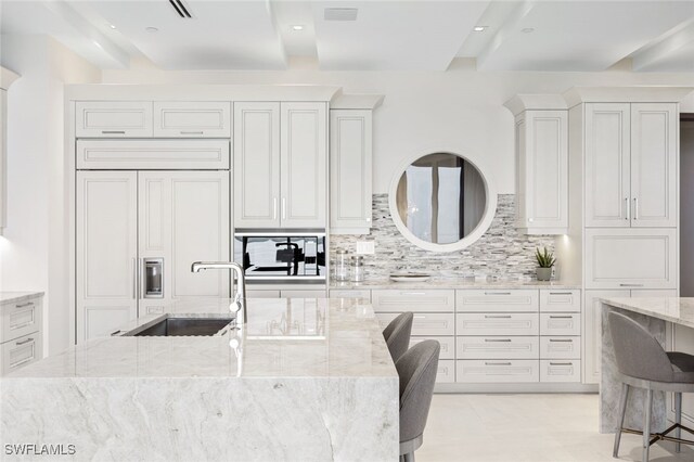 kitchen with paneled fridge, a kitchen breakfast bar, light stone countertops, tasteful backsplash, and sink