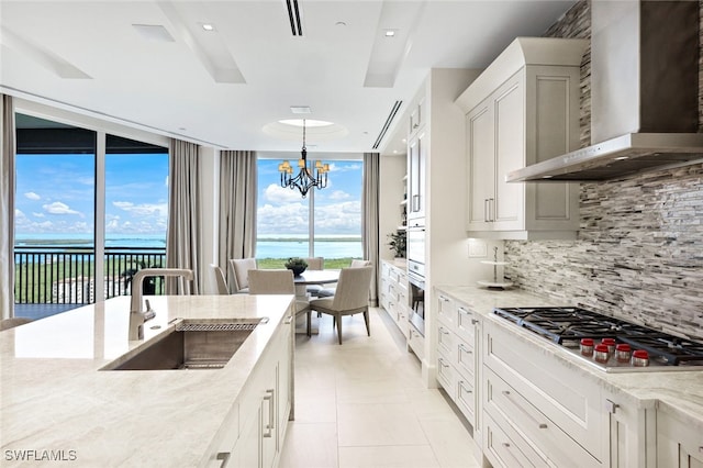 kitchen featuring stainless steel gas cooktop, backsplash, decorative light fixtures, sink, and wall chimney exhaust hood