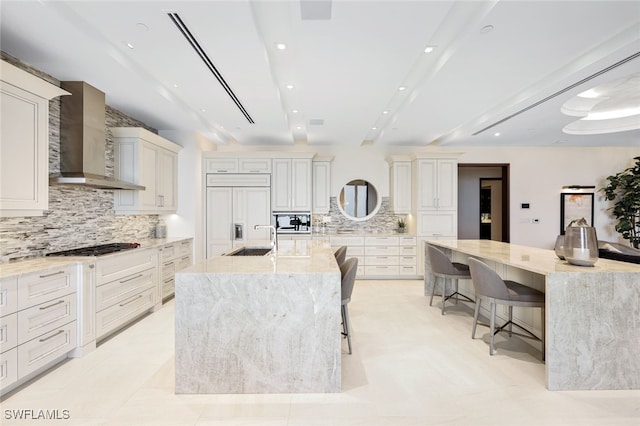 kitchen with a spacious island, wall chimney exhaust hood, built in appliances, a kitchen bar, and tasteful backsplash