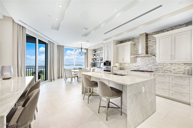 kitchen featuring wall chimney range hood, a kitchen bar, light stone counters, and an island with sink