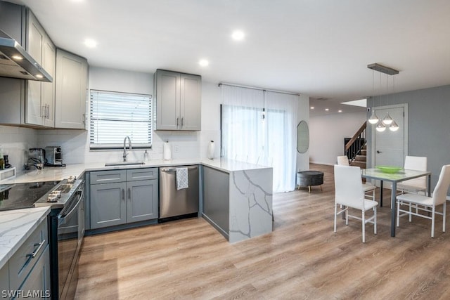 kitchen with sink, stainless steel appliances, wall chimney range hood, decorative light fixtures, and gray cabinets