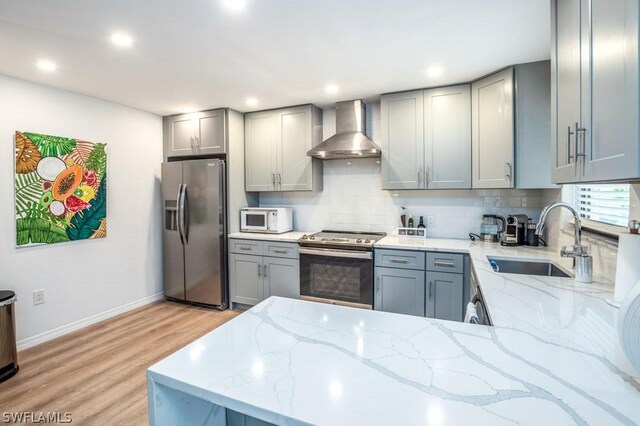 kitchen featuring light stone countertops, wall chimney range hood, stainless steel appliances, and a sink