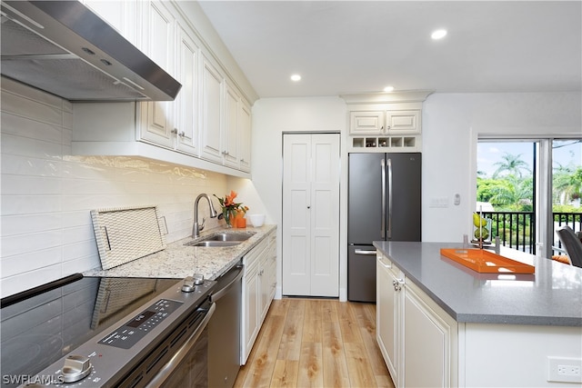 kitchen with wall chimney range hood, sink, appliances with stainless steel finishes, white cabinetry, and light wood-type flooring