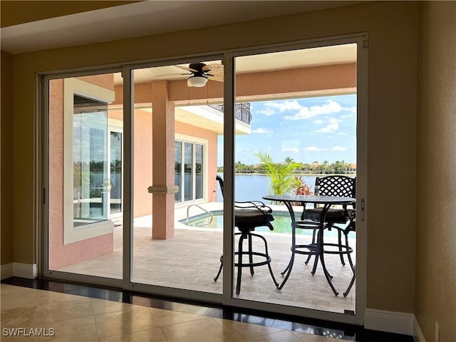 doorway with a water view, tile patterned floors, and ceiling fan