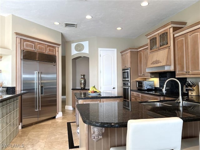 kitchen with premium range hood, a kitchen island, built in appliances, light tile patterned flooring, and decorative backsplash