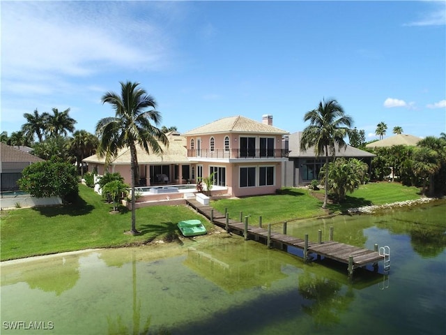 back of property with a water view, a balcony, and a lawn