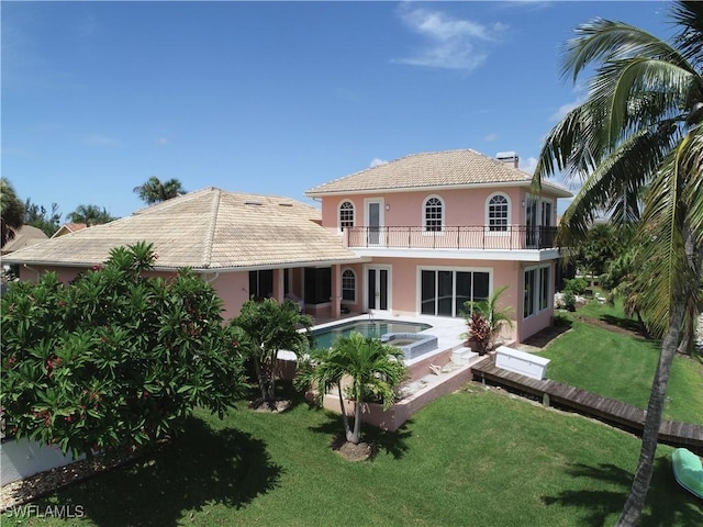 back of house with a balcony, a yard, and a swimming pool with hot tub