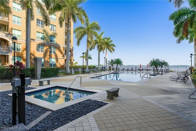 view of pool featuring a hot tub, a patio, and a water view