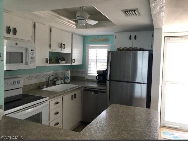 kitchen with a raised ceiling, ceiling fan, white appliances, and white cabinets