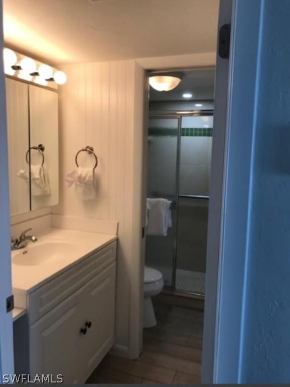 bathroom featuring hardwood / wood-style floors, vanity, a shower with shower door, and toilet