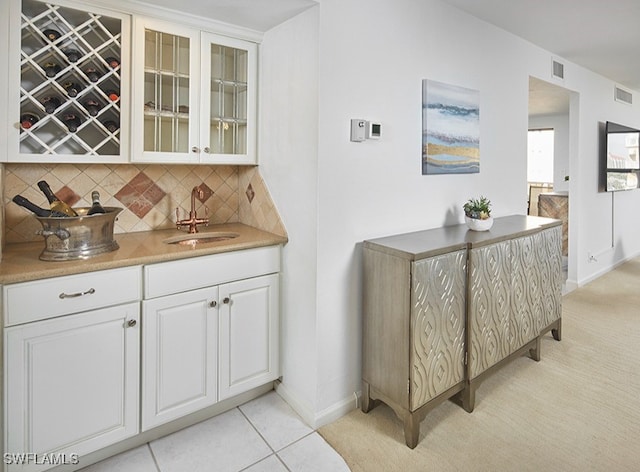 bar with tasteful backsplash, white cabinetry, sink, and light tile patterned floors