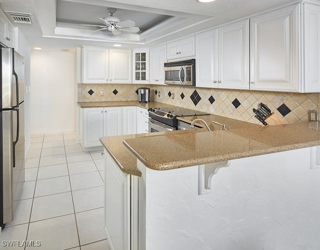 kitchen with a raised ceiling, white cabinetry, a breakfast bar area, kitchen peninsula, and stainless steel appliances