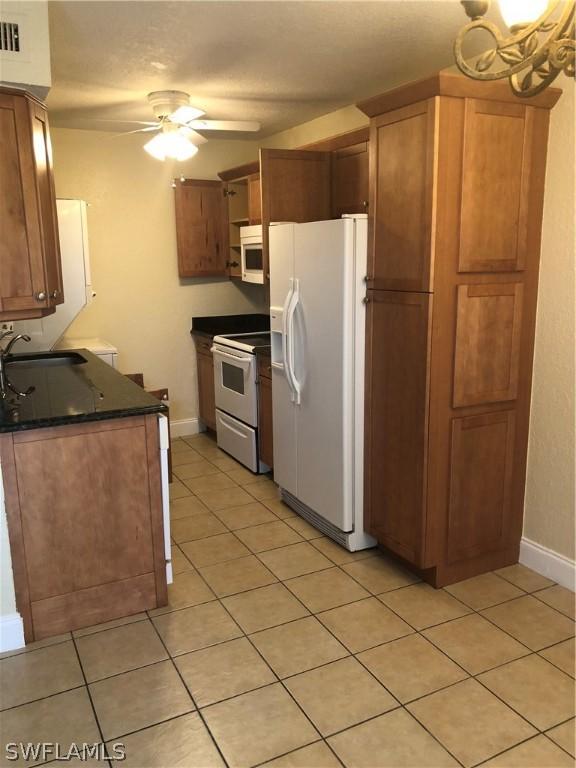 kitchen featuring dark stone counters, ceiling fan, white appliances, sink, and light tile patterned floors