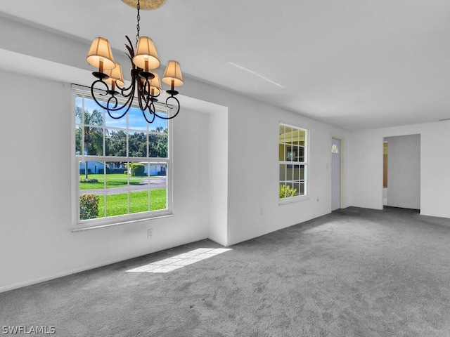 carpeted empty room featuring plenty of natural light and an inviting chandelier