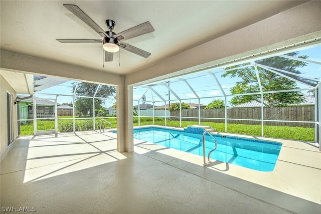 view of pool featuring a yard, glass enclosure, ceiling fan, and a patio area