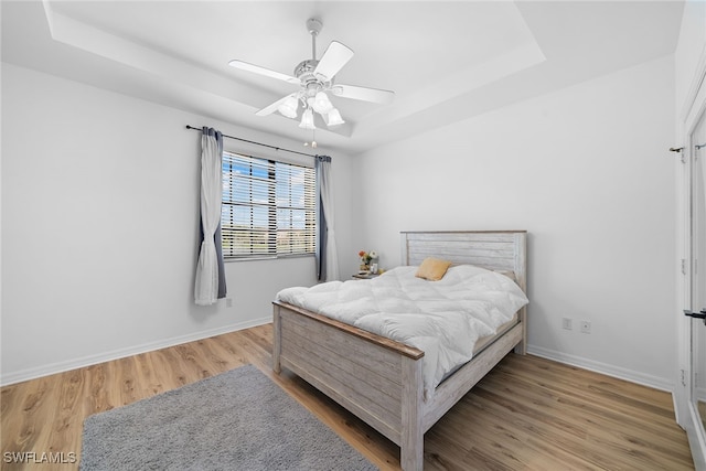 bedroom featuring a raised ceiling, ceiling fan, and hardwood / wood-style flooring