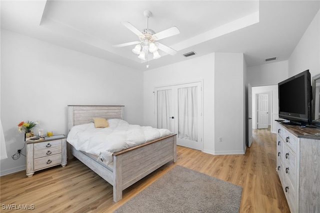 bedroom with ceiling fan, a closet, light hardwood / wood-style floors, and a tray ceiling