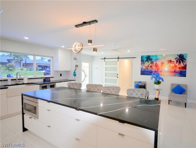 kitchen featuring tasteful backsplash, decorative light fixtures, stainless steel microwave, a barn door, and white cabinets