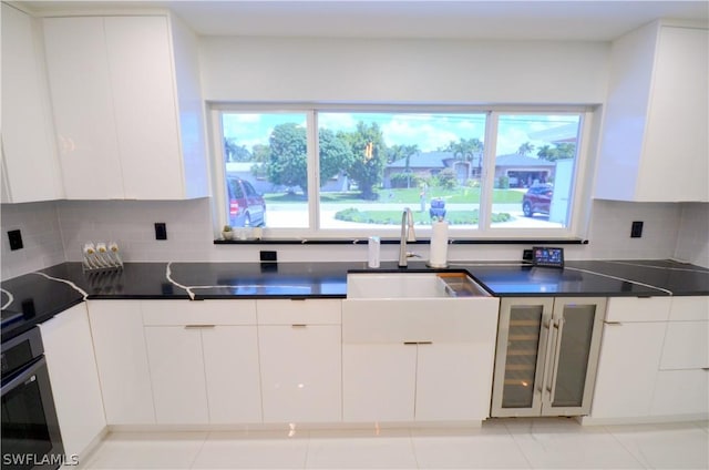 kitchen featuring white cabinetry, stainless steel oven, sink, and decorative backsplash