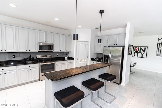 kitchen featuring hanging light fixtures, white cabinetry, a kitchen island with sink, and appliances with stainless steel finishes