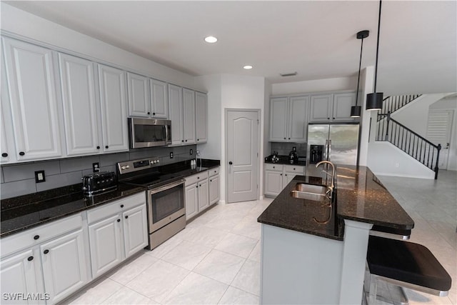 kitchen with stainless steel appliances, a sink, hanging light fixtures, an island with sink, and a kitchen bar