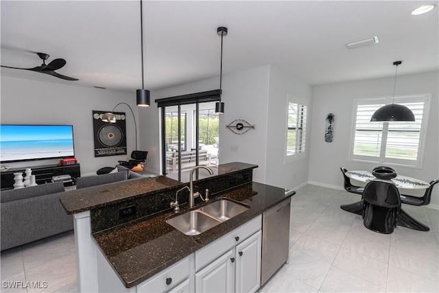 kitchen featuring a sink, white cabinetry, open floor plan, hanging light fixtures, and dark stone counters