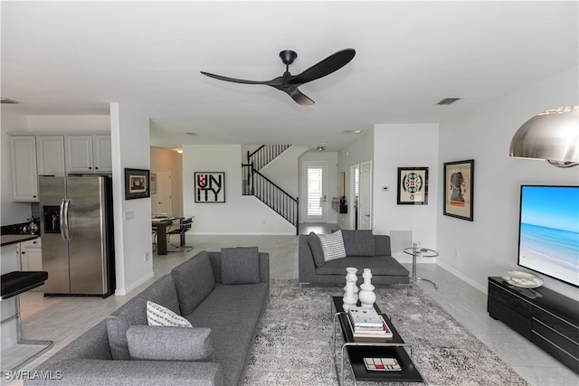 living room with baseboards, stairs, visible vents, and ceiling fan