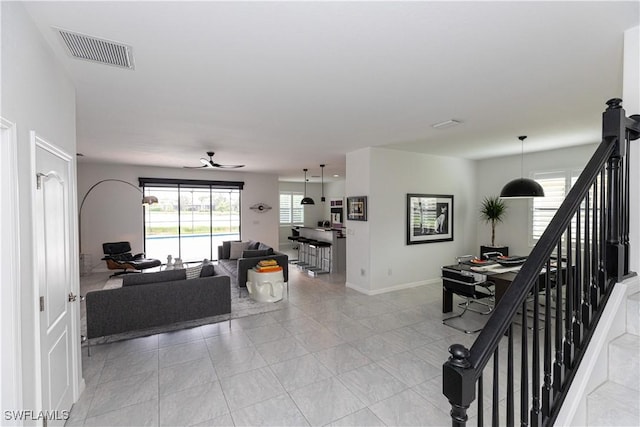 living room with light tile patterned floors, visible vents, ceiling fan, baseboards, and stairs