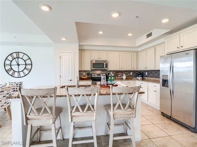 kitchen with stainless steel appliances, decorative backsplash, a kitchen bar, light tile patterned floors, and a kitchen island with sink