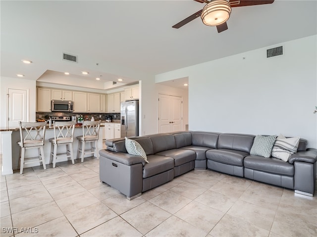 tiled living room with ceiling fan and a raised ceiling