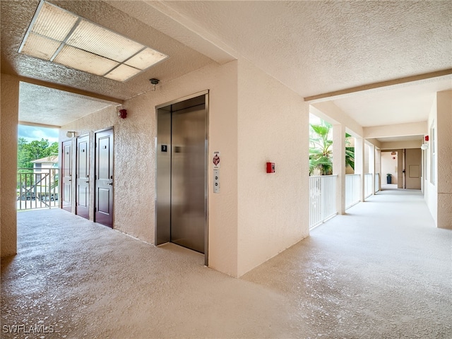 hallway with elevator, a textured ceiling, and a healthy amount of sunlight