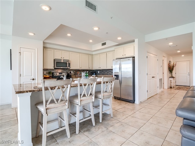 kitchen with appliances with stainless steel finishes, tasteful backsplash, a kitchen breakfast bar, an island with sink, and dark stone countertops