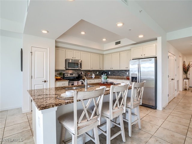 kitchen with dark stone counters, stainless steel appliances, tasteful backsplash, a breakfast bar, and a kitchen island with sink