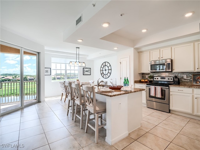 kitchen with dark stone countertops, backsplash, a kitchen island, hanging light fixtures, and appliances with stainless steel finishes