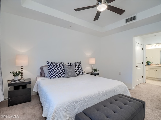 carpeted bedroom with a tray ceiling, connected bathroom, and ceiling fan