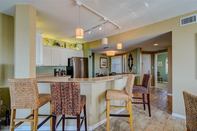 kitchen with white cabinetry, stainless steel fridge, a kitchen breakfast bar, and decorative light fixtures