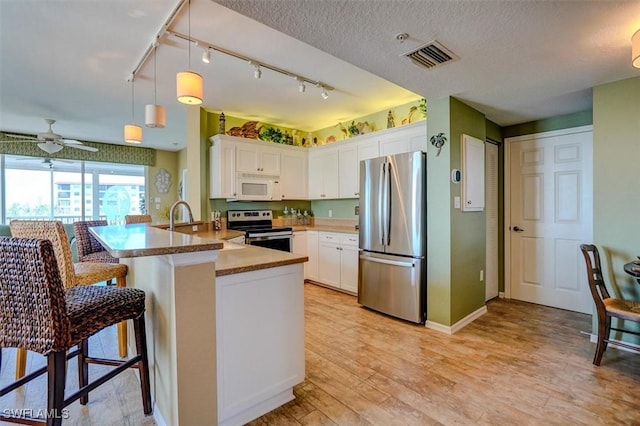 kitchen with a breakfast bar, appliances with stainless steel finishes, white cabinetry, hanging light fixtures, and kitchen peninsula