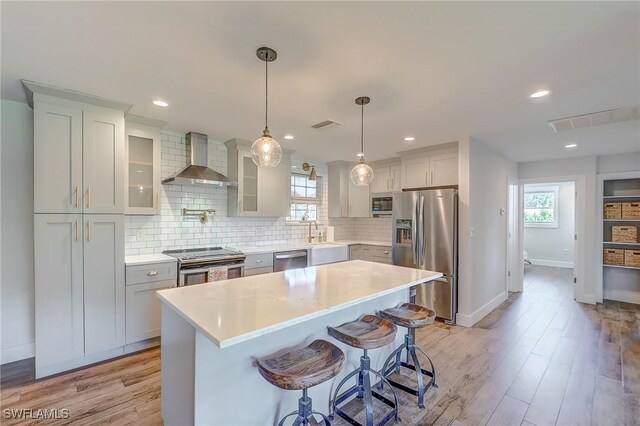 kitchen featuring stainless steel appliances, light wood-type flooring, a kitchen island, backsplash, and wall chimney range hood